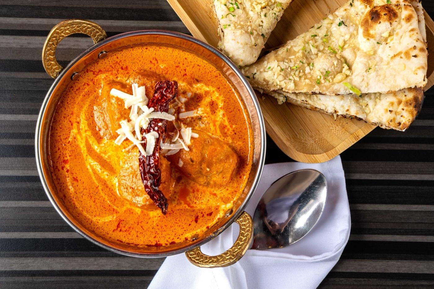 Creamy Halal butter chicken in a copper kadhai served with garlic naan at India 101 in Irving, TX