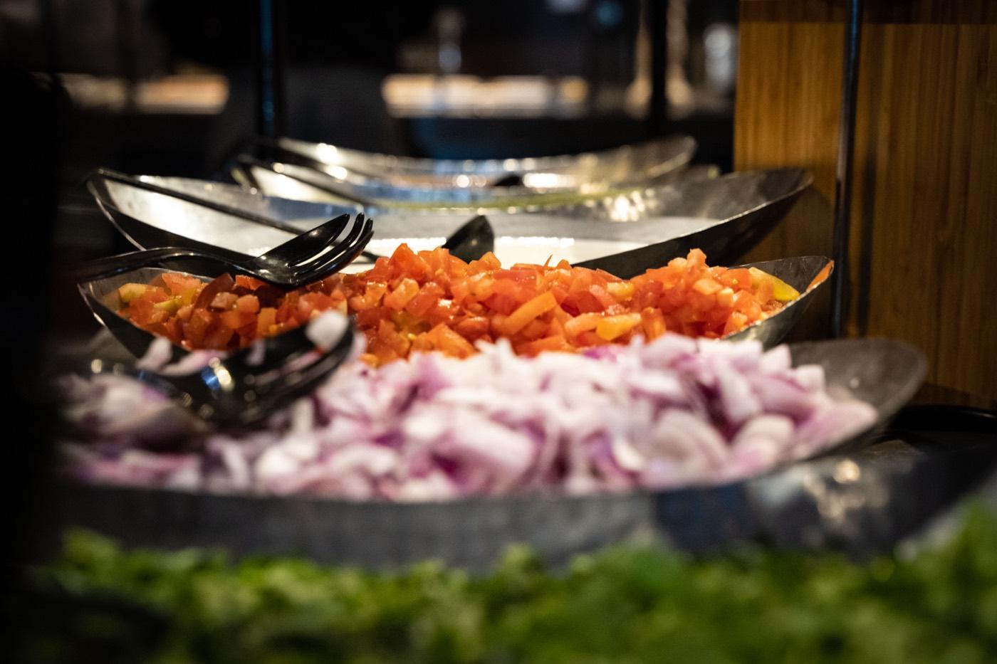 Buffet boats of diced tomatoes and red onions over greens at India 101 in Irving, TX