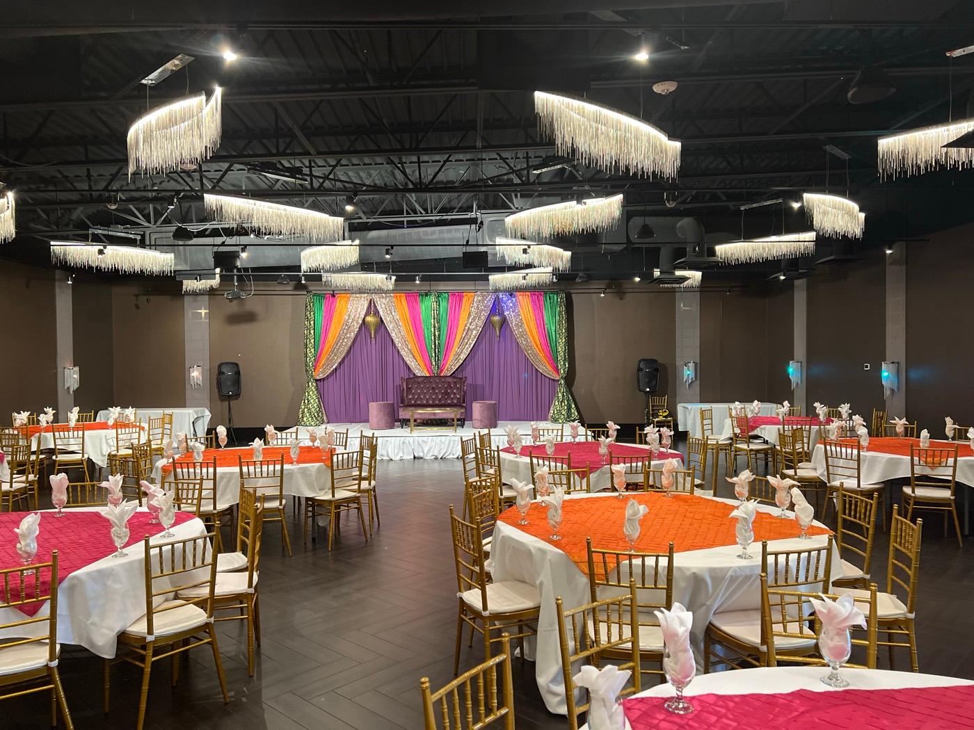 Colorful mehndi sangeet stage with orange and pink table linens at India 101 banquet hall in Irving, TX