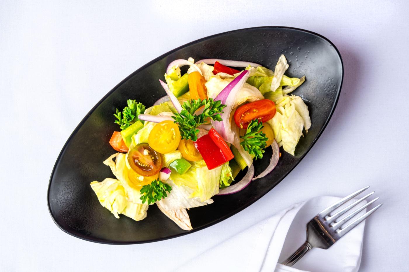 Fresh garden salad on a black oval plate with lettuce, tomatoes and onion at India 101 in Irving, TX