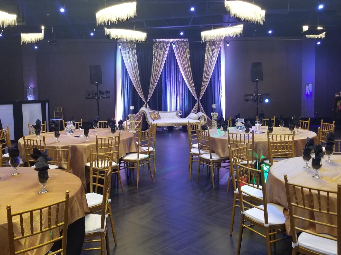 Banquet hall set with gold Chiavari chairs and draped sweetheart stage at India 101 banquet hall in Irving, TX