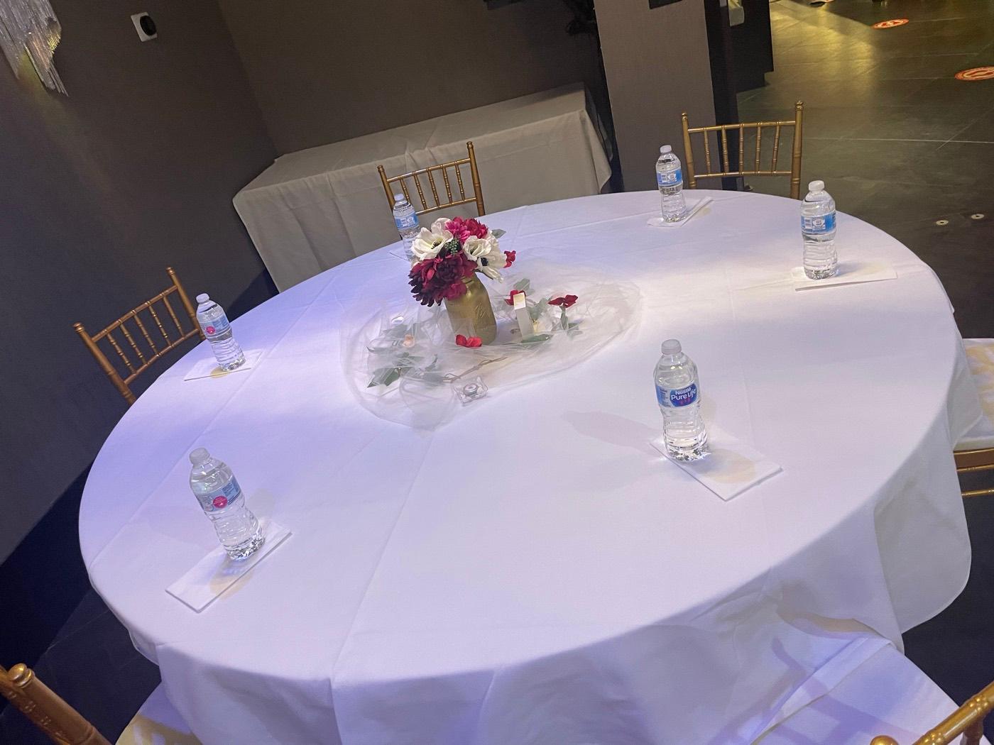 Round guest table with burgundy floral centerpiece and place settings at India 101 banquet hall in Irving, TX