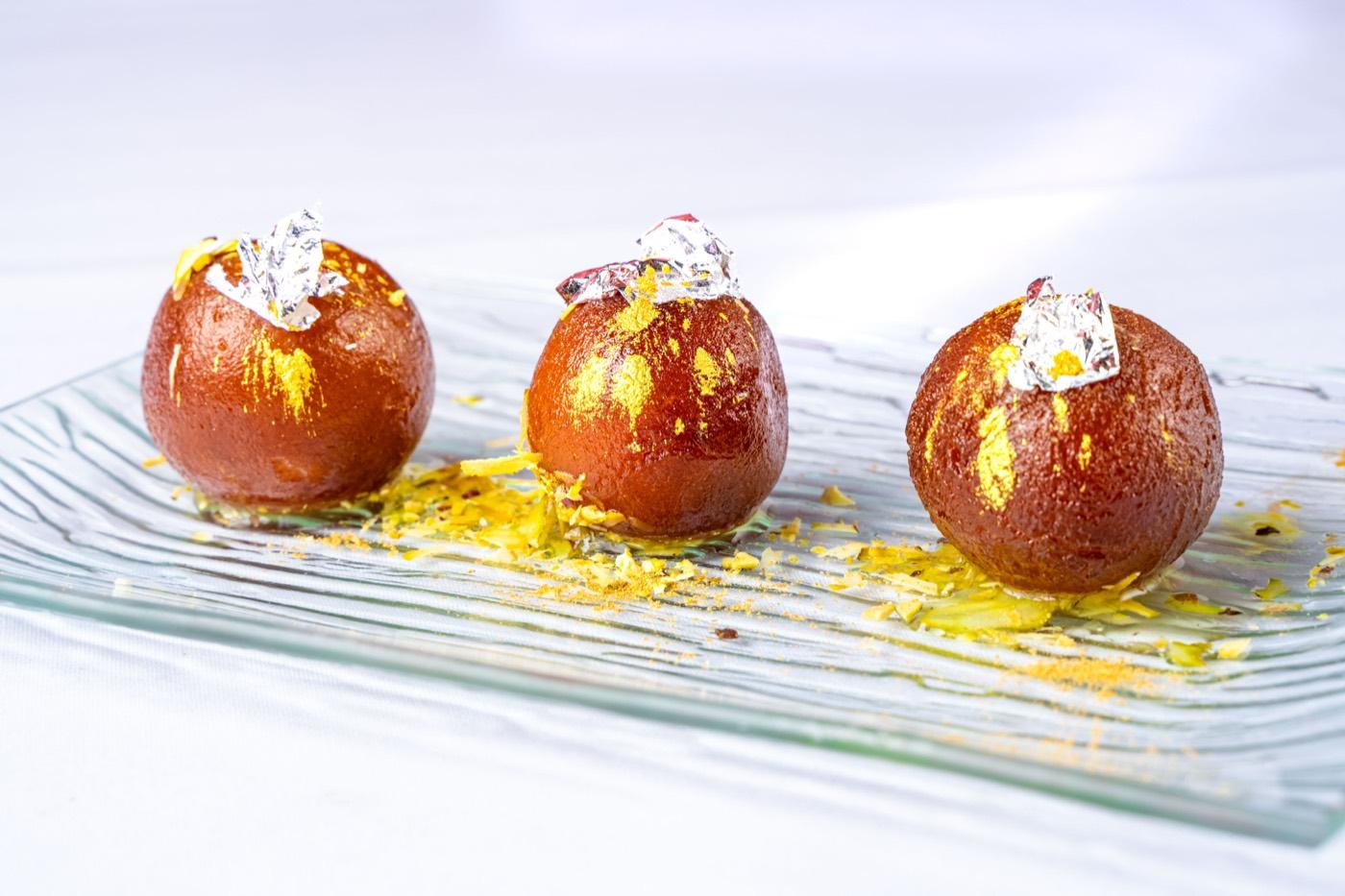 Gulab jamun garnished with silver leaf on a textured glass plate at India 101 in Irving, TX