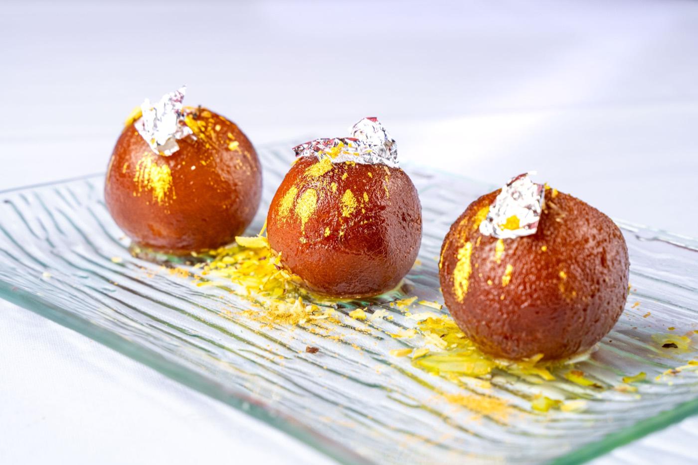 Three glossy gulab jamun with silver leaf on a glass platter at India 101 in Irving, TX