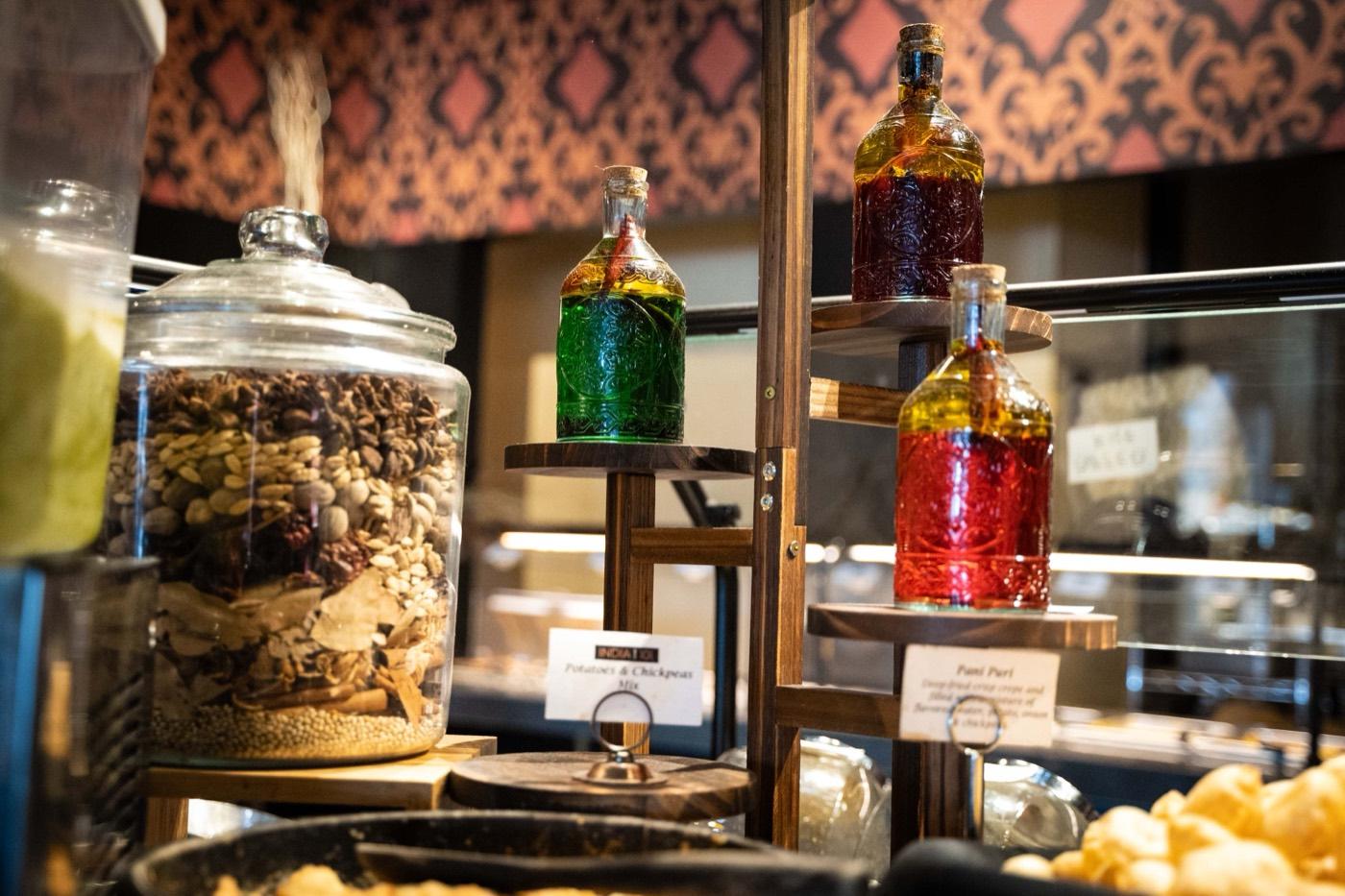 Chaat station with spice jars and colored infused-water bottles labeled Pani Puri at India 101 in Irving, TX