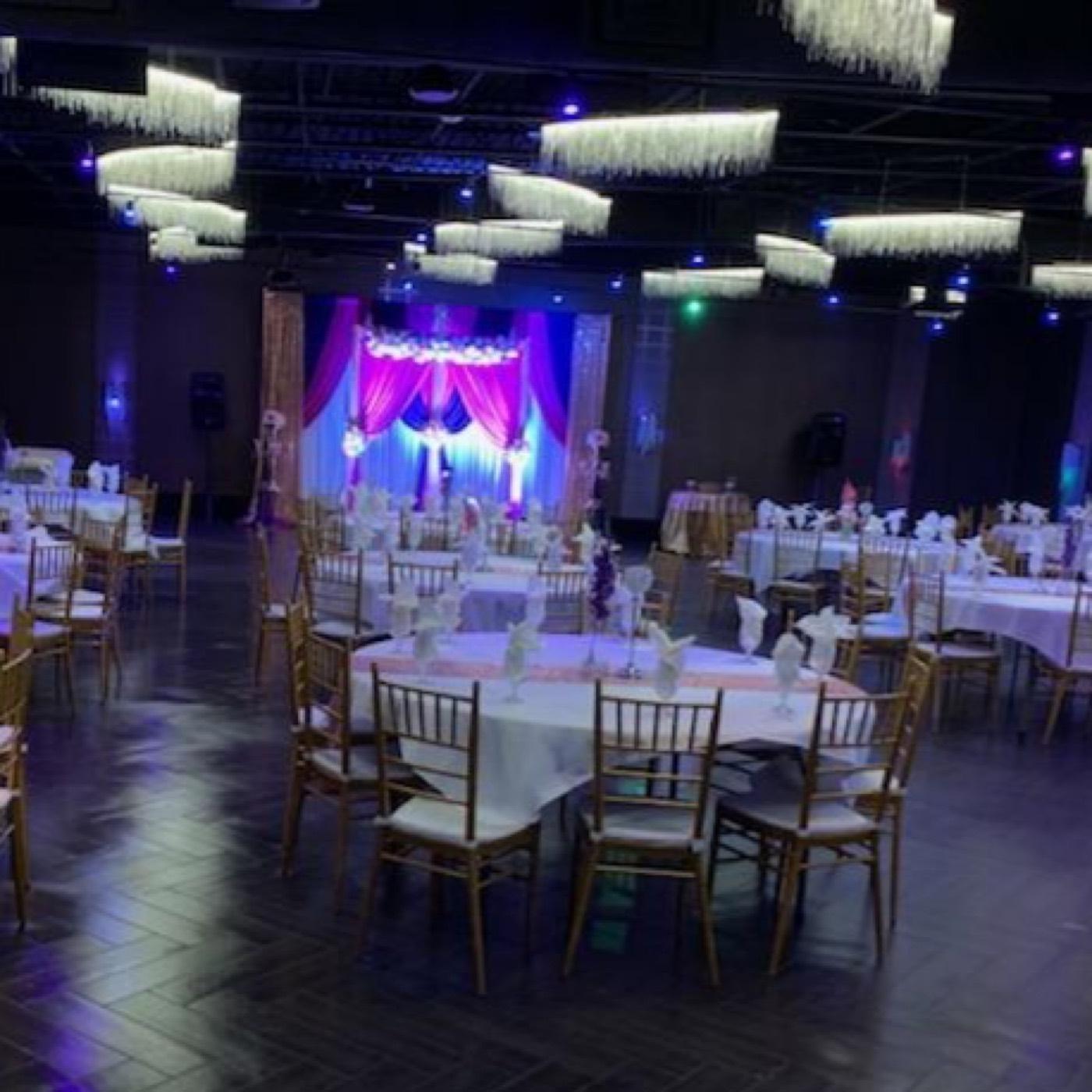 Banquet hall in purple lighting with draped stage and round tables at India 101 banquet hall in Irving, TX