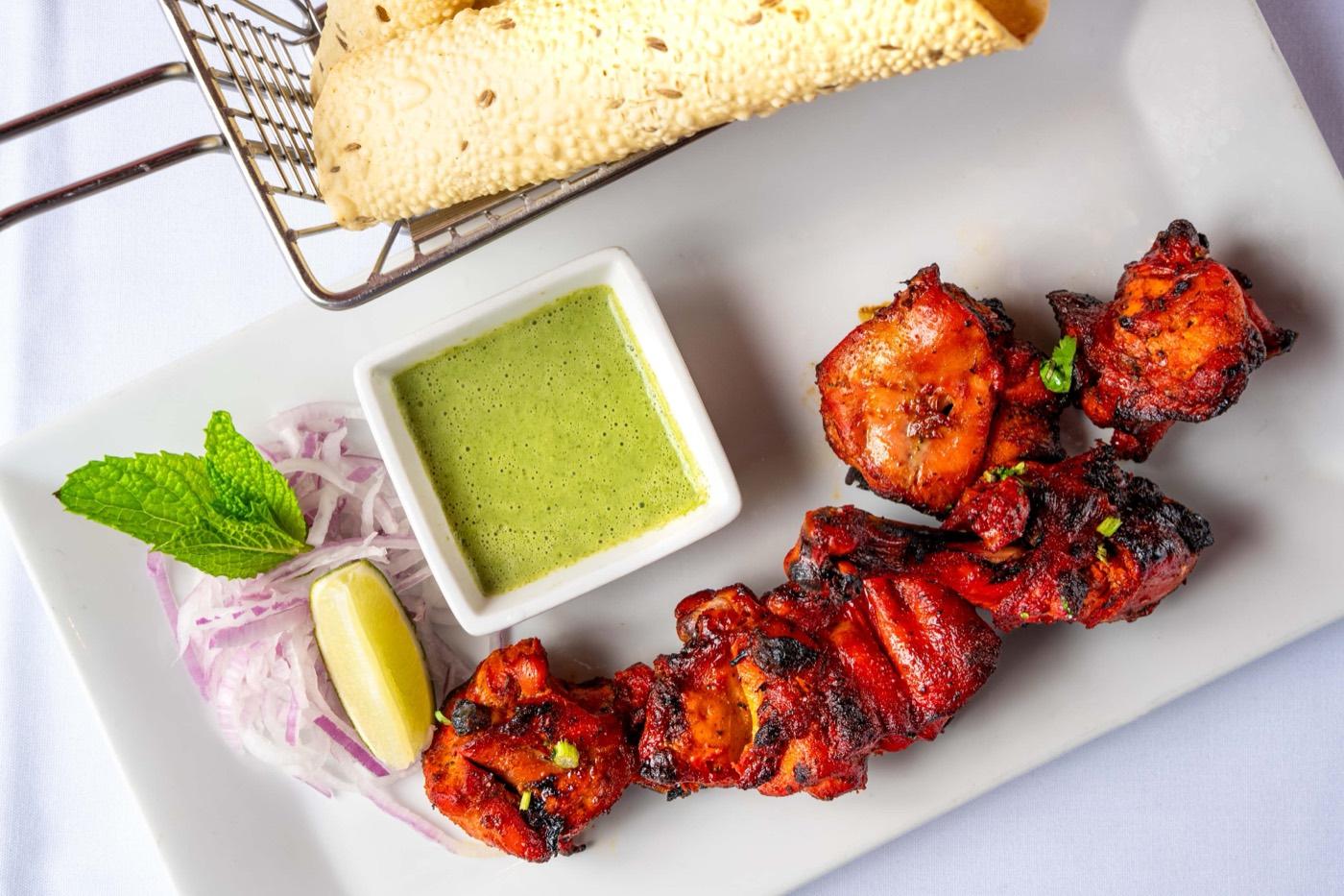 Char-grilled tandoori chicken pieces with green chutney, onions, and papad at India 101 in Irving, TX