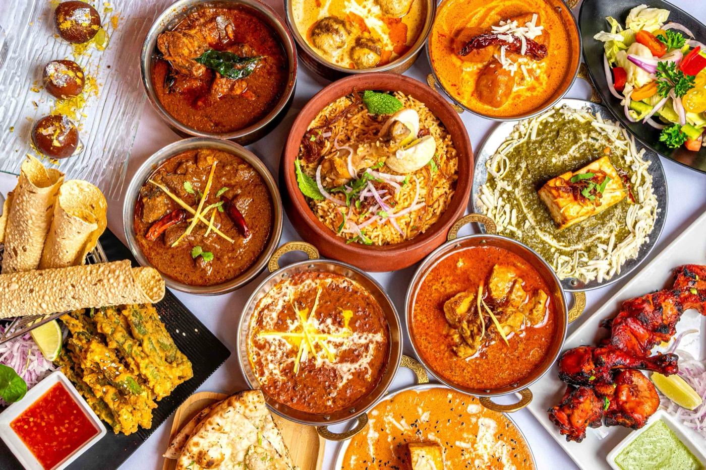Overhead spread of Halal Indian dishes including biryani, tandoori chicken, paneer and curries at India 101 in Irving, TX